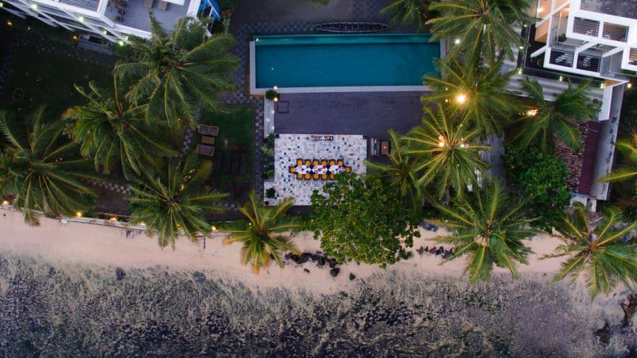 Aerial view of a resort pool and palms directly beside a sandy beach
