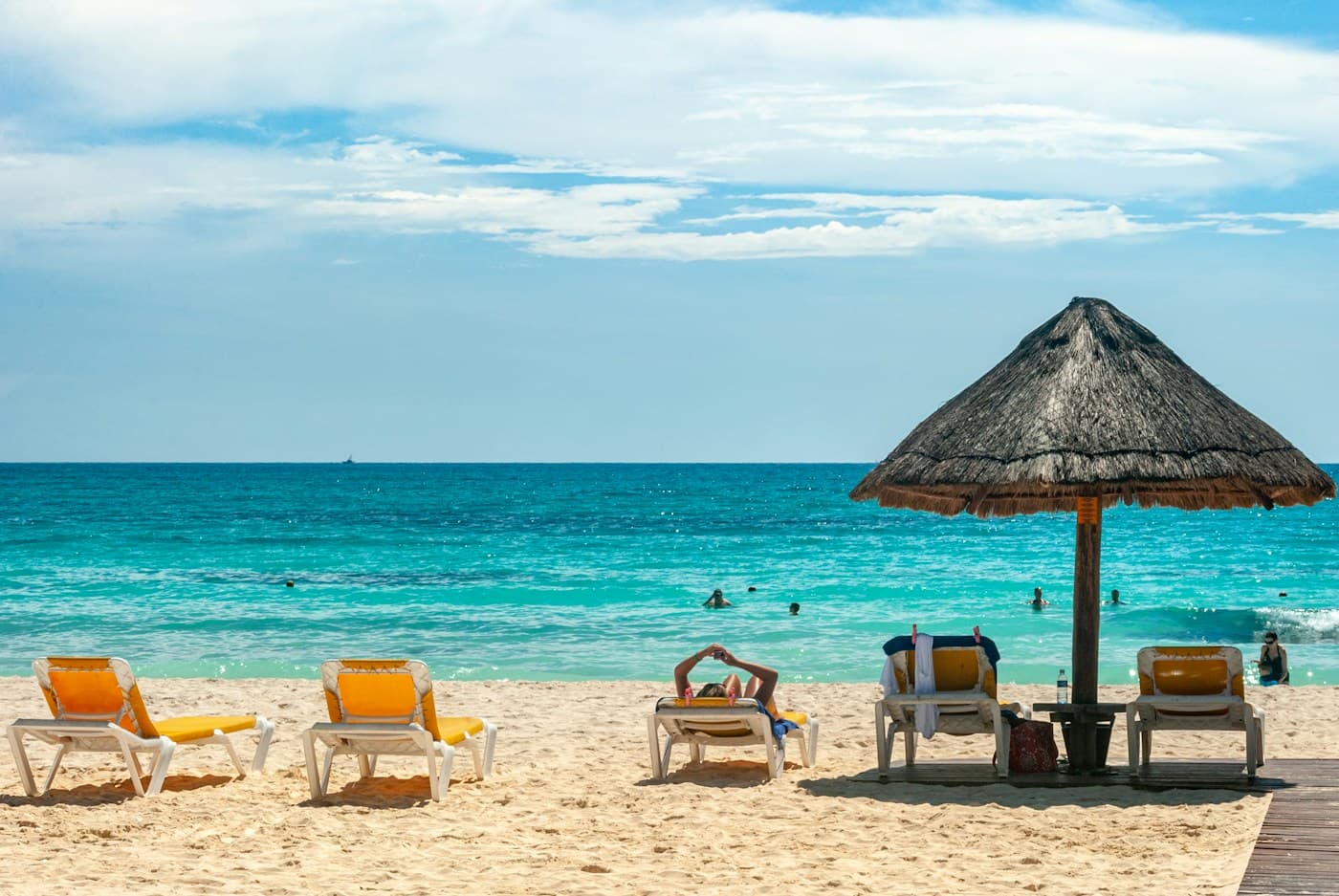 Thatched beach umbrella and yellow loungers beside turquoise water in Cancún, Mexico