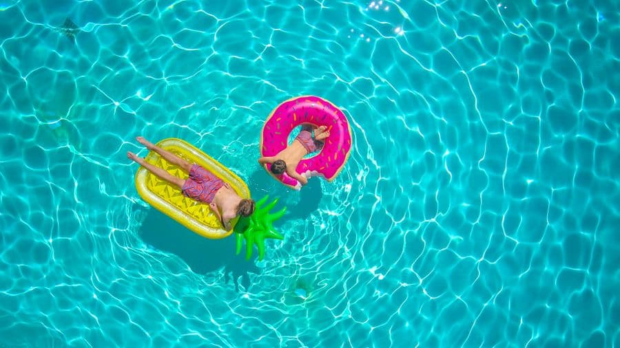 Two children floating on colorful inflatables in a sunny swimming pool
